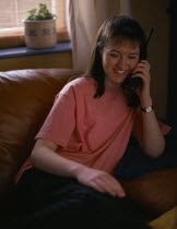 Smiling teenage girl sat on sofa using cordless telephone Model Released ELT & Educational use only