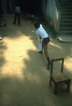 Young boys playing Cricket in street using a wooden chair as stumps