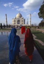 The Taj Mahal with women in saris walking towards it beside the pool