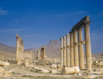 Monumental Arch  columns and fallen masonry with fort on hillside beyond.  Palmyra