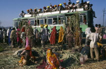 Over crowded bus with people on the roof and hanging out of windows.