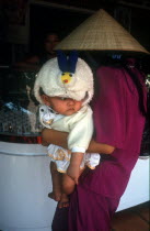 Woman in a straw hat holding a baby as she looks at a shop display in Tay Ninh market.