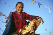Smiling female Tibetan refugee sitting amongst prayer flags on roof of temple