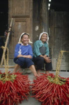 Two smiling female chilli vendors sitting on a pavement behind their chillies