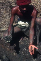 Gem miner displaying gems in one hand and unpanned mud in other.