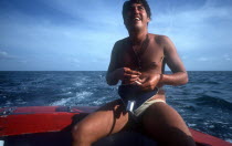 Man sitting at the back of a boat putting bait on the end of a fishing hook