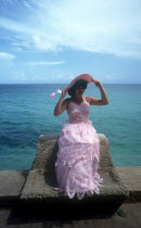 Girl sitting on sea wall wearing a pink party dress for her 15th birthday