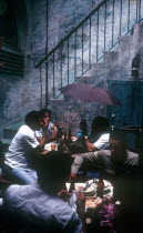 Bodequita del Medio Bar with people sitting at tables in an alley by a stairway and one man holding an umbrella
