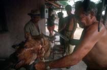 Man standing at spit carving a whole roasted pig with a large knife