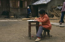 Young girl doing homework at desk in farmyard.