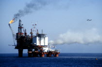 Worker in a hard hat standing on the deck watching flames from burning off gas over the North sea