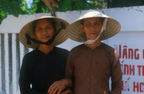 Mother and daughter standing with linked arms  wearing traditional straw hats.