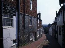 View down cobbled old street with cottage housing and a street sign showing directions towards the Ann of Cleves House and The Priory.