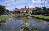 Wisley Royal Horticultural Society Garden. View across formal pond with water lilies towards the Tudor style half timbered main entrance building.