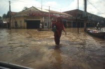 Woman holding young child whilst wading through flooded street