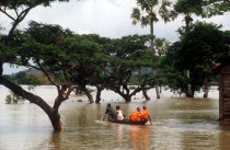 Two Budhist monks in a canoe being rowed through flood water on Route 1 from Neak Long to Svay Rieng.