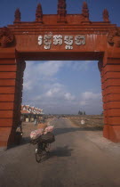 Man on a bicycle crossing the border between Cambodia and Vietnam underneath large archway.