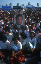 Crowds awaiting the arrival of Sihanouk outside the Royal Palace  many holding flags and posters.
