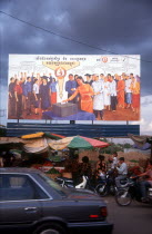Election poster with line of stalls selling fruit along the roadside in front.