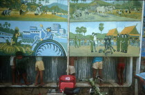 Anti Khmer Rouge posters with line of children behind so only their legs can be seen.