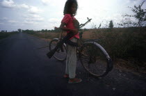 Ten year old girl standing on the Route 6 roadway beside her bicycle holding an AK47.