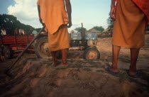 Building construction.  Cropped view of monks with hoe watching tractor and trailer.