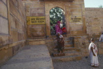 Women and children at Jain temple passing sign indicating bath room.  Cult images are washed daily by priests and lay worshippers bath before worship.