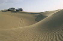 Dune driving.  Two jeeps on ridge of wind rippled sand dune.