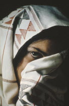 Young woman with face half hidden by head dress.