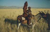 Himba nomad woman and child in traditional leather clothing crossing the Marienfluss on donkey in Kaokolan