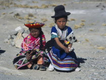 Two young children sitting on the ground with one holding a lamb
