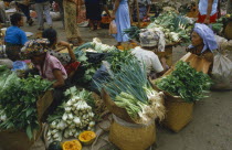 Market sellers sitting around baskets of green vegetables.