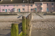 View of old fishermens cottages along the waterfront from the beach with a groyne in the foreground.