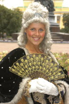Portrait of a woman in historical dress wearing a wig and holding a fan