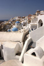View over white town architecture with occasional blue domesThira Fira Santorini