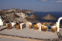 Terrace with tables and chairs under thatch umbrellas overlooking coastal cliffs Thira