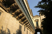 View along decorative architectural detail of enclosed balcony leading along the side of the building toward an archway