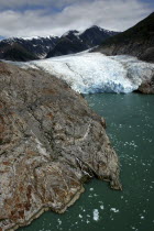 View over rocky edged waterway toward icy slope and mountain peaks beyond