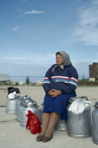 Woman sitting on milk cans waiting for ferry on the Baltic Coast.