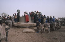 Crowds of people with donkeys collecting water from well.