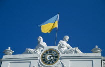 Ukranian flag flying from town hall above clock face and between two statues.
