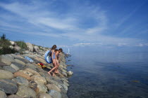 Group of young girls wlking down stone sea defence into water off the Baltic coast.