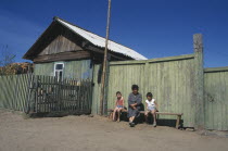 Buryat woman and children outside painted wooden fence of house.  The Buryat are of Mongolian descent and are the largest ethnic minority group in Siberia.