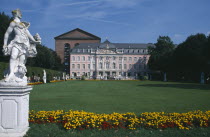 Episcopal Palace.  Exterior facade and visitors with statue and flower bed in the foreground.