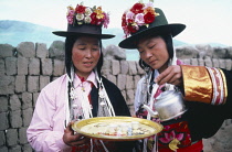 Women of Tu nationality and Lamaist Buddhist Yellow Hat sect preparing traditional welcome of three small glasses of alcoholic drink.