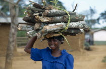 Young woman carrying bundle of firewood on her head.