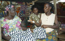 Woman purchasing length of batik dyed cloth with fish design from market vendor.money transactionbuying