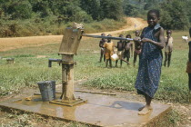 Young girl using village hand pump to draw water.