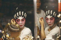 Performer in Chinese opera applying make up  reflected in mirror at side.