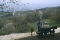 Dog walkers in conversation in park above city.